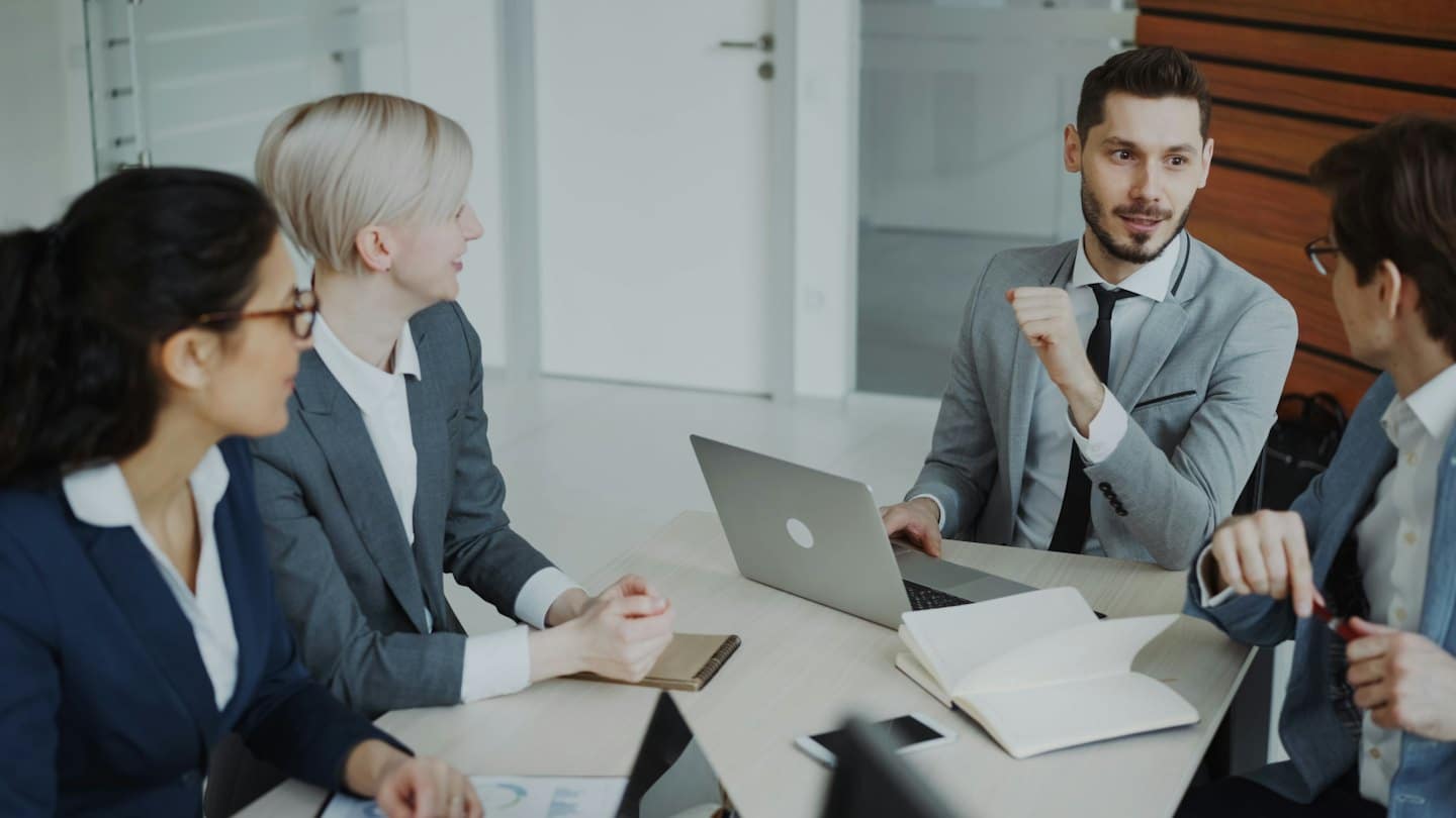 Services Professionals discuss business around a conference table with laptops and documents.