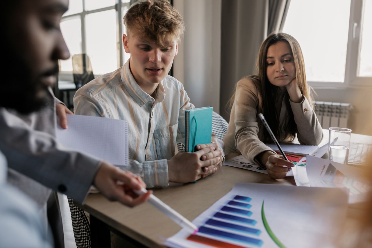 Services A diverse team of young professionals engaged in a business meeting analyzing graphs and data.